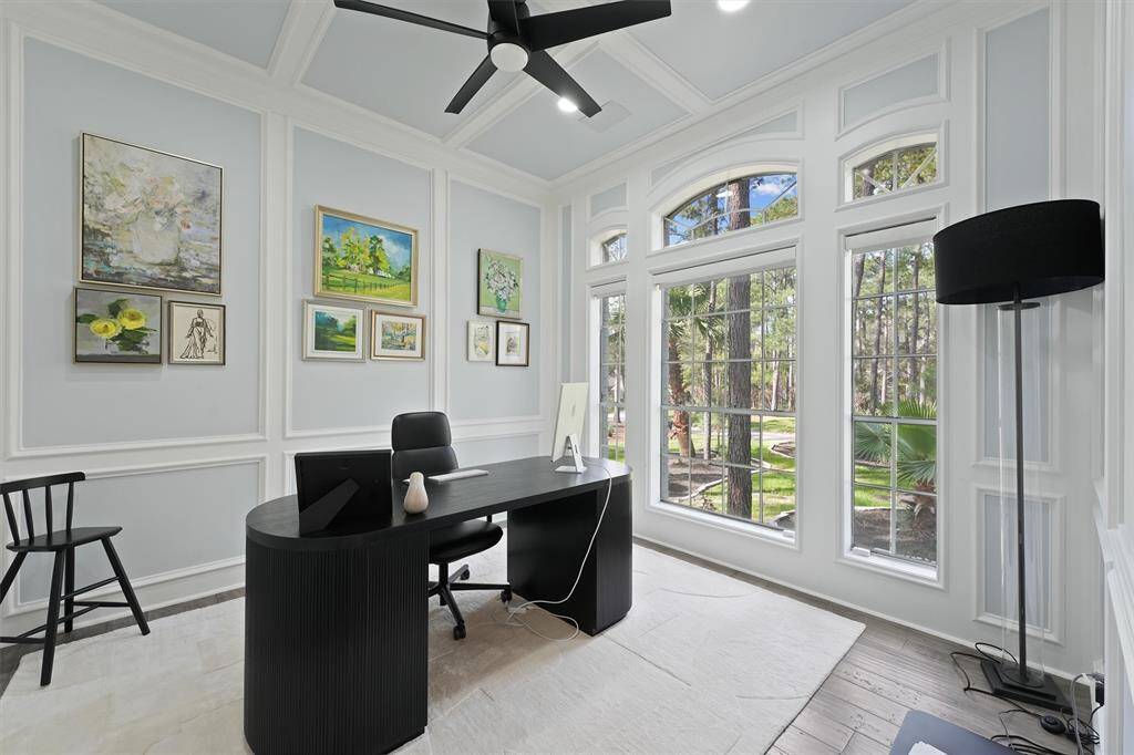 This bright and stylish home office features large windows with scenic views, elegant paneling, modern furnishings, and ample natural light, creating an inviting workspace.