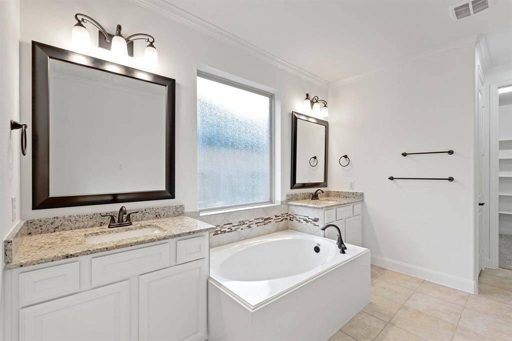 The spacious primary bathroom boasts a luxurious large bathtub, double sink vanities with ample counter space, and beautiful tile flooring, creating a perfect retreat for relaxation and convenience.