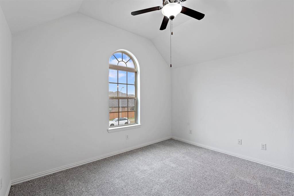 This charming bedroom boasts a high sloped ceiling, an elegant arched window that lets in plenty of natural light, and cozy carpet for added comfort.