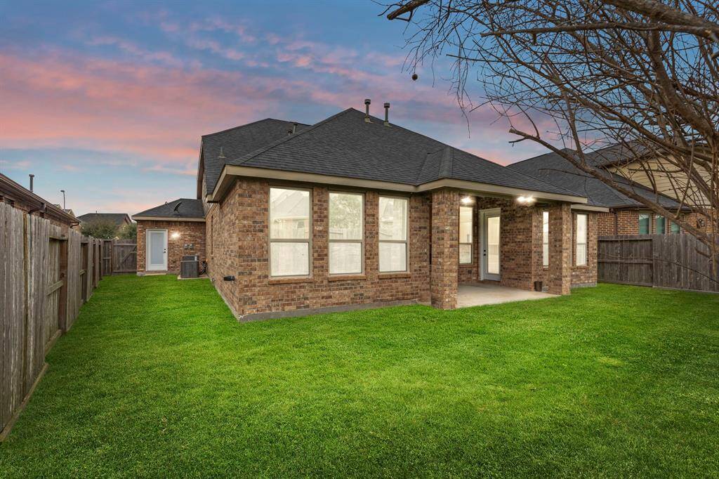 The spacious fenced backyard boasts a vibrant green lawn and a charming covered patio—ideal for enjoying the outdoors in comfort and style.
