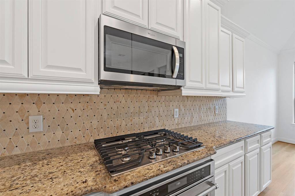 This close-up showcases the stylish gas stovetop with a built-in microwave above, complemented by a custom backsplash that adds a touch of elegance to the kitchen.