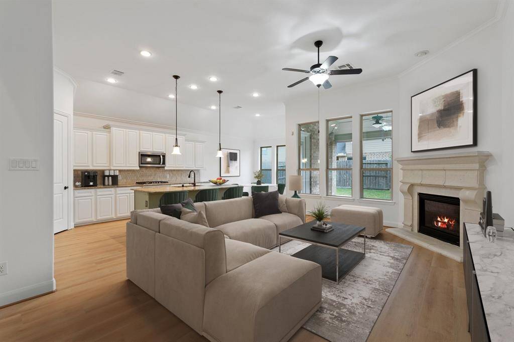 The inviting living room seamlessly flows into the kitchen, featuring a stylish ceiling fan, multiple windows for abundant natural light, and a cozy gas log fireplace—perfect for relaxation and entertaining! *Virtually Staged*