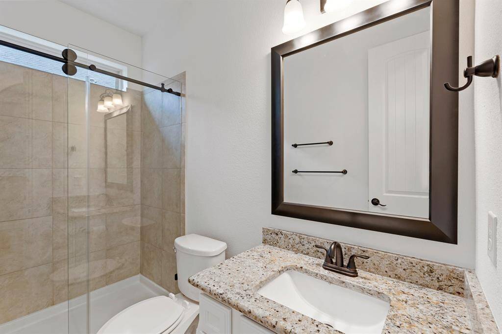 This stylish bathroom features a sleek shower/tub combo with a sliding glass door, complemented by a white sink vanity with a luxurious granite countertop!
