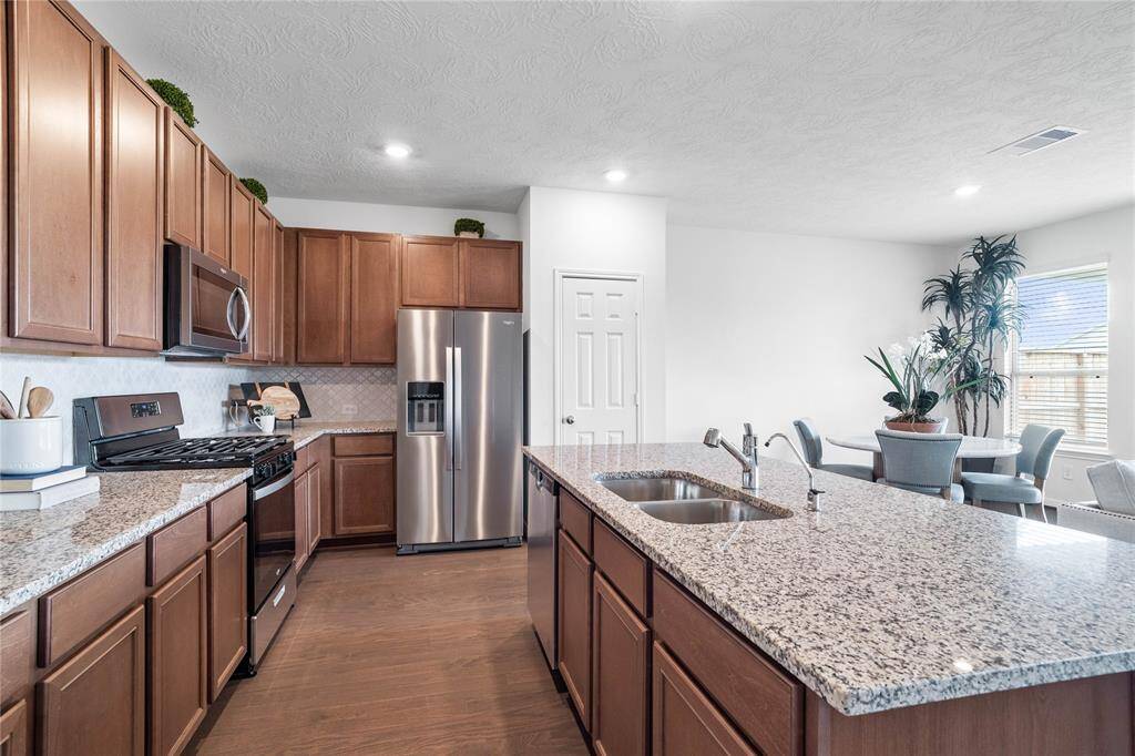This spacious kitchen features high ceilings, stained wood cabinets, granite countertops, SS appliances, modern tile backsplash, recessed lighting, and pantry all overlooking your huge family room.