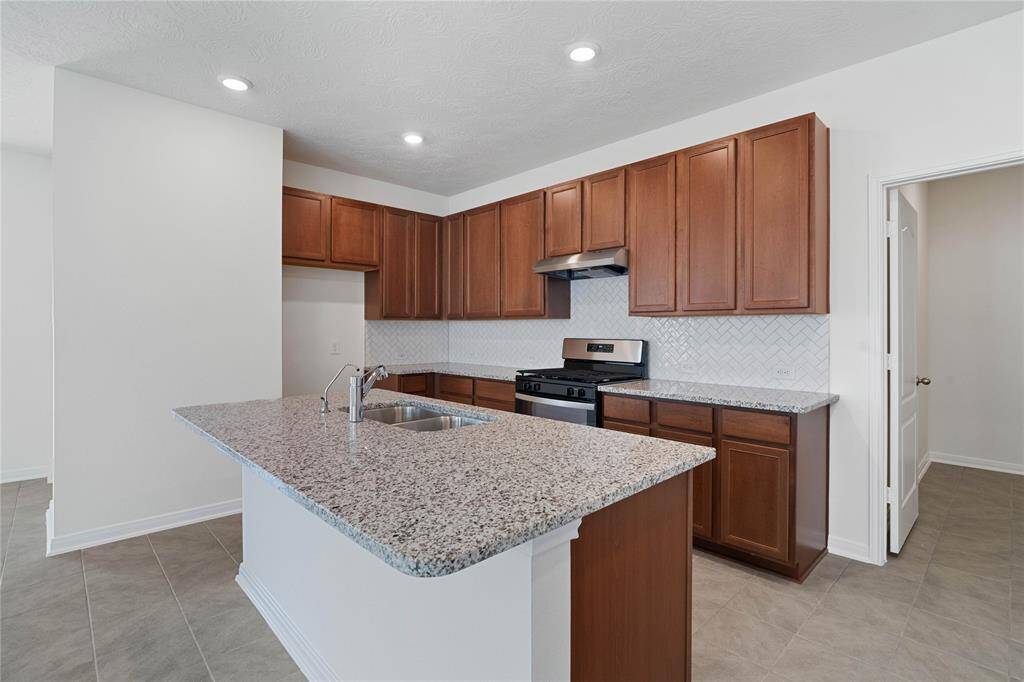 This spacious kitchen features high ceilings, stained wood cabinets, granite countertops, SS appliances, modern tile backsplash, and recessed lighting, all overlooking your huge family room.