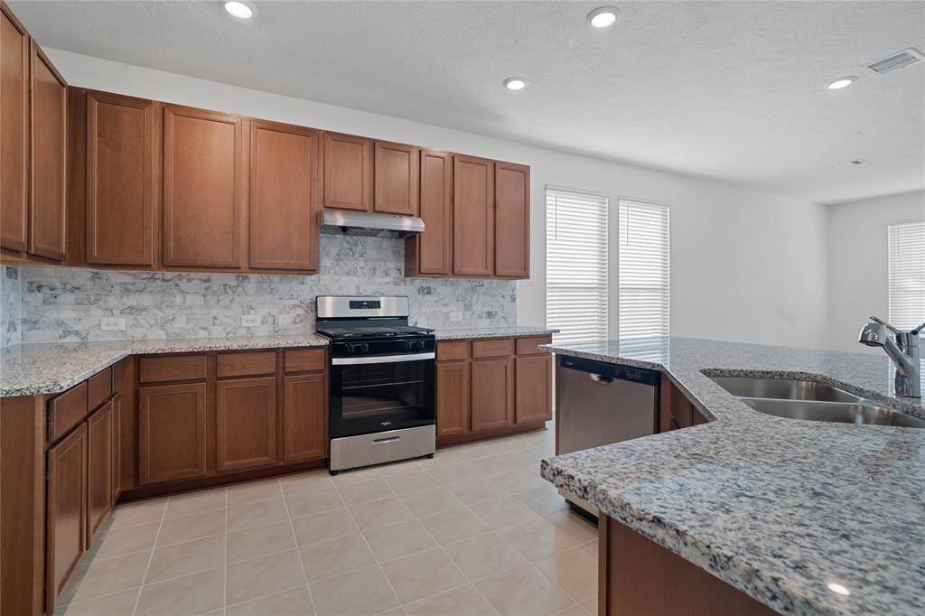 This spacious kitchen features high ceilings, stained wood cabinets, granite countertops, SS appliances, modern tile backsplash, and recessed lighting, all overlooking your huge family room.