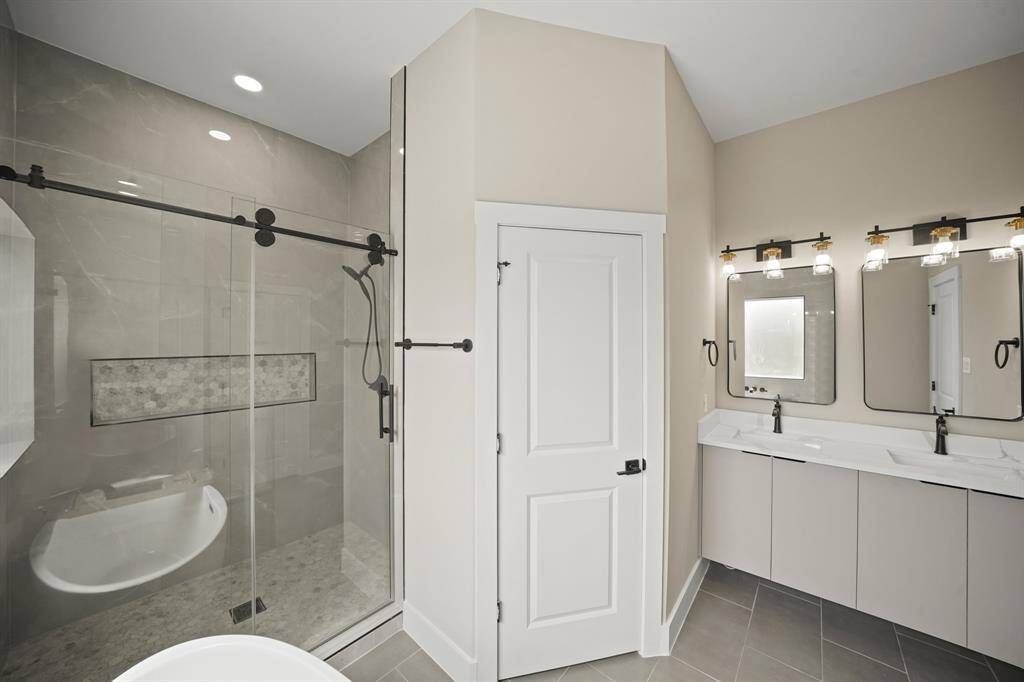 Check out the primary bathroom! Highlighted by an amazing glass enclosed shower with gorgeous tile, recessed lighting, double sinks, quartz countertops, and framed mirrors.