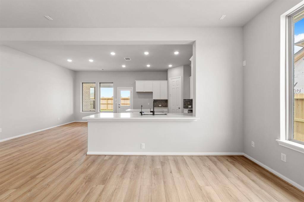 This light and bright kitchen features a large quartz island, white cabinets, a large sink overlooking your family room, recessed lighting, and beautiful backsplash.