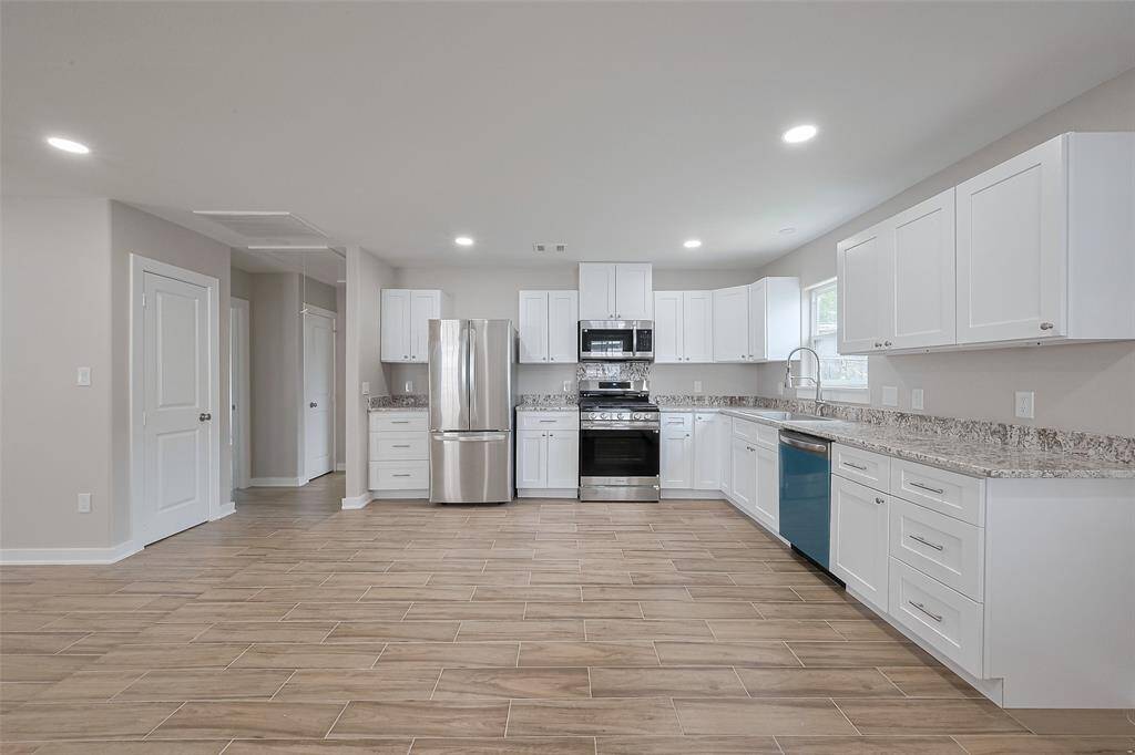 This photo showcases a modern kitchen with white cabinets, granite countertops, and stainless steel appliances. The space is open and bright, featuring recessed lighting and wood-look tile flooring.