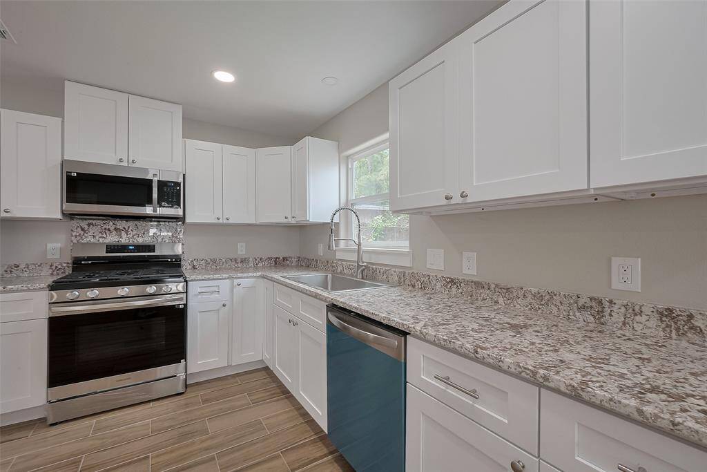 This kitchen features modern appliances, white cabinetry, and granite countertops. It offers ample space with a sleek design, a large sink, and a window for natural light.