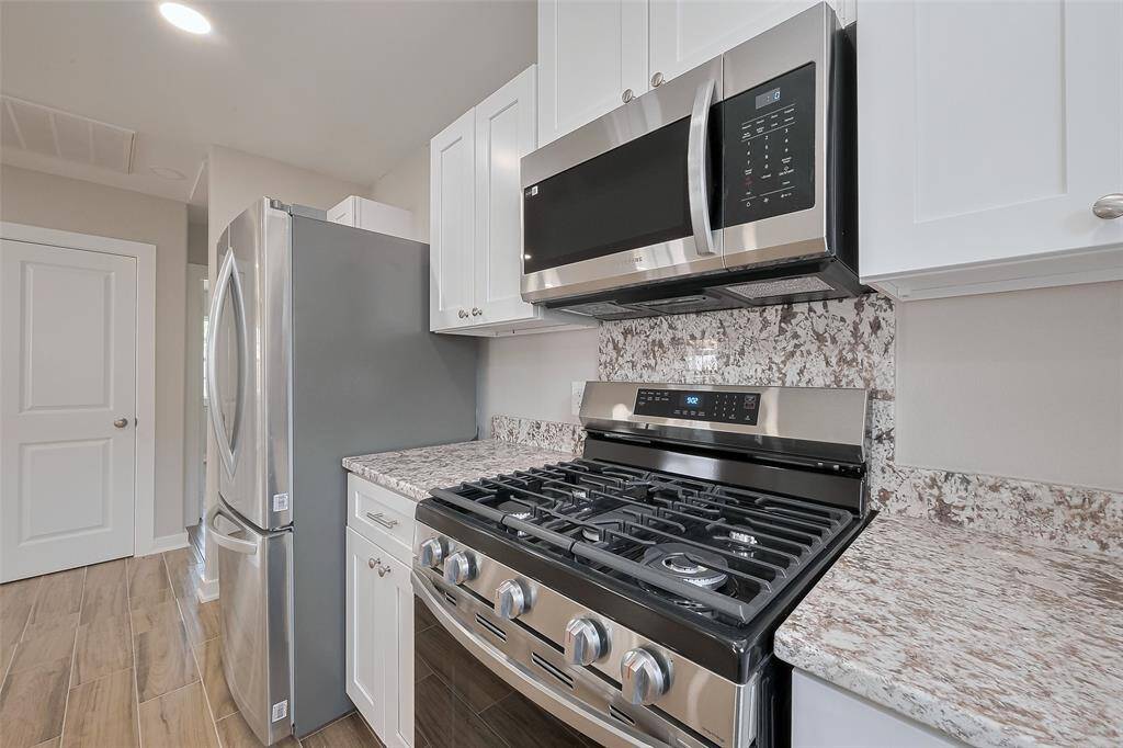 This modern kitchen features stainless steel appliances, including a gas stove and built-in microwave, complemented by granite countertops and sleek white cabinetry.