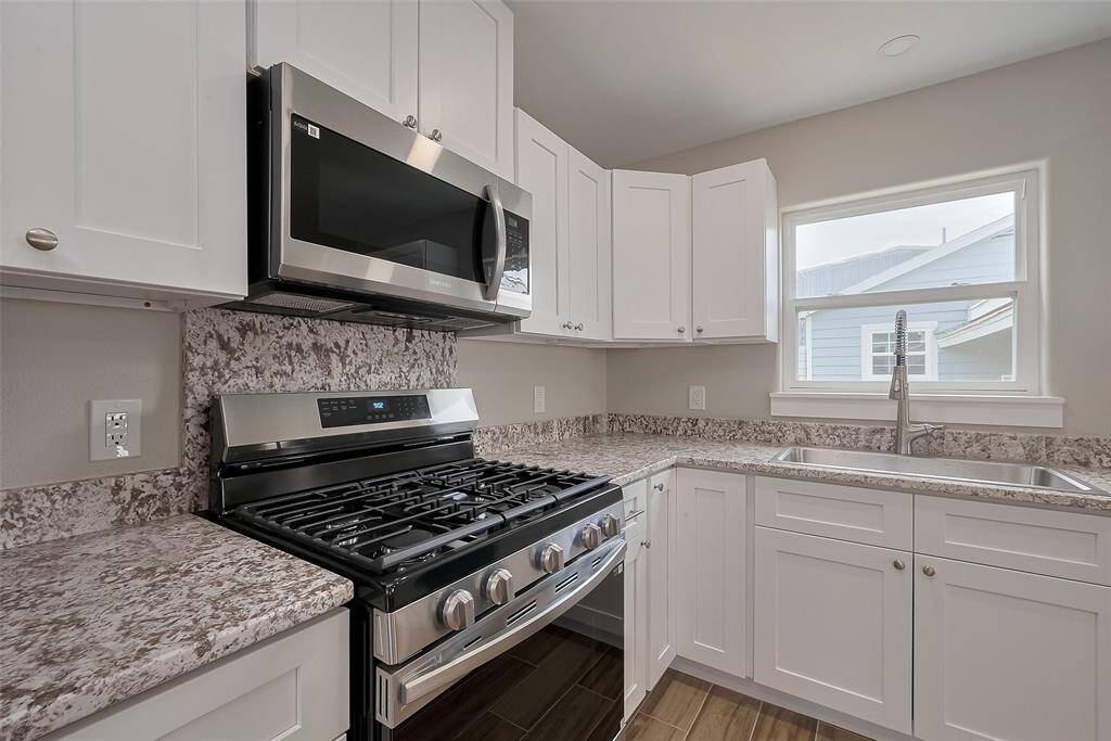 This kitchen features modern stainless steel appliances, including a gas stove and microwave. It has sleek granite countertops, white cabinetry, and a bright window over the sink, providing a clean and contemporary look.