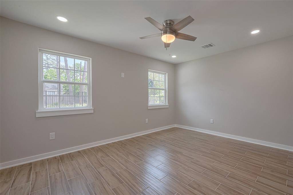 This room features a bright, airy space with neutral walls and wood-look tile flooring. It includes two windows for natural light, recessed lighting, and a ceiling fan for comfort.