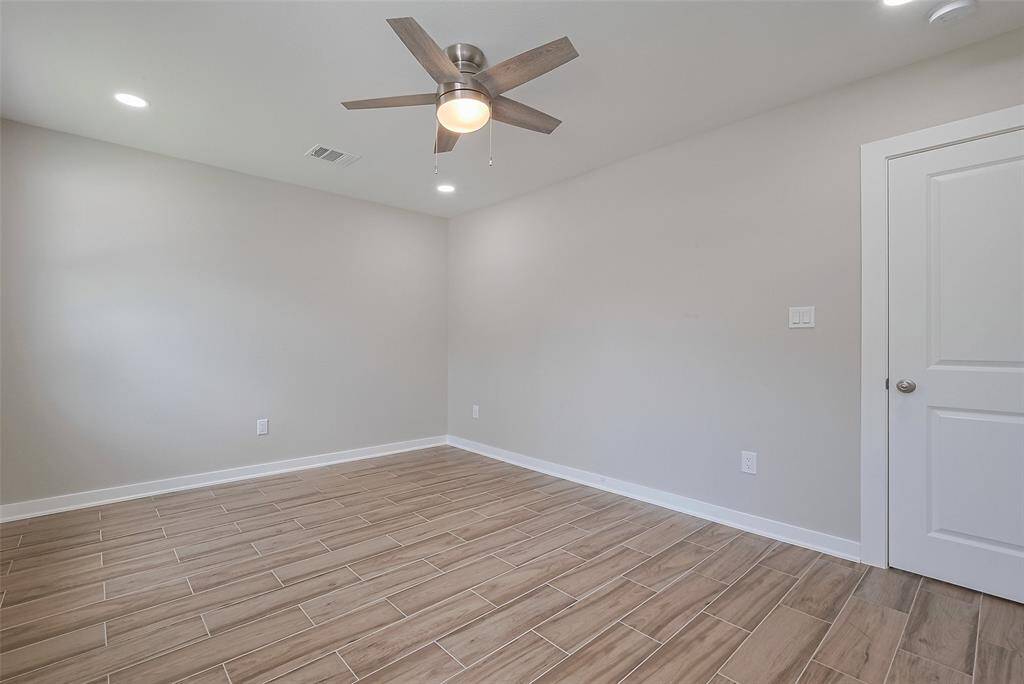 This photo shows a bright, empty room with neutral-colored walls, wood-look tile flooring, and a modern ceiling fan. Recessed lighting and a white door add to the clean, contemporary feel. Perfect for customization.