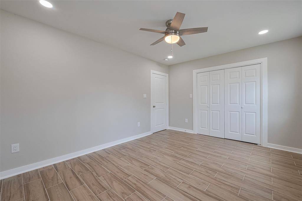This room features light wood-look tile flooring, neutral walls, and recessed lighting. It includes a ceiling fan and a double-door closet, offering a clean and modern look.