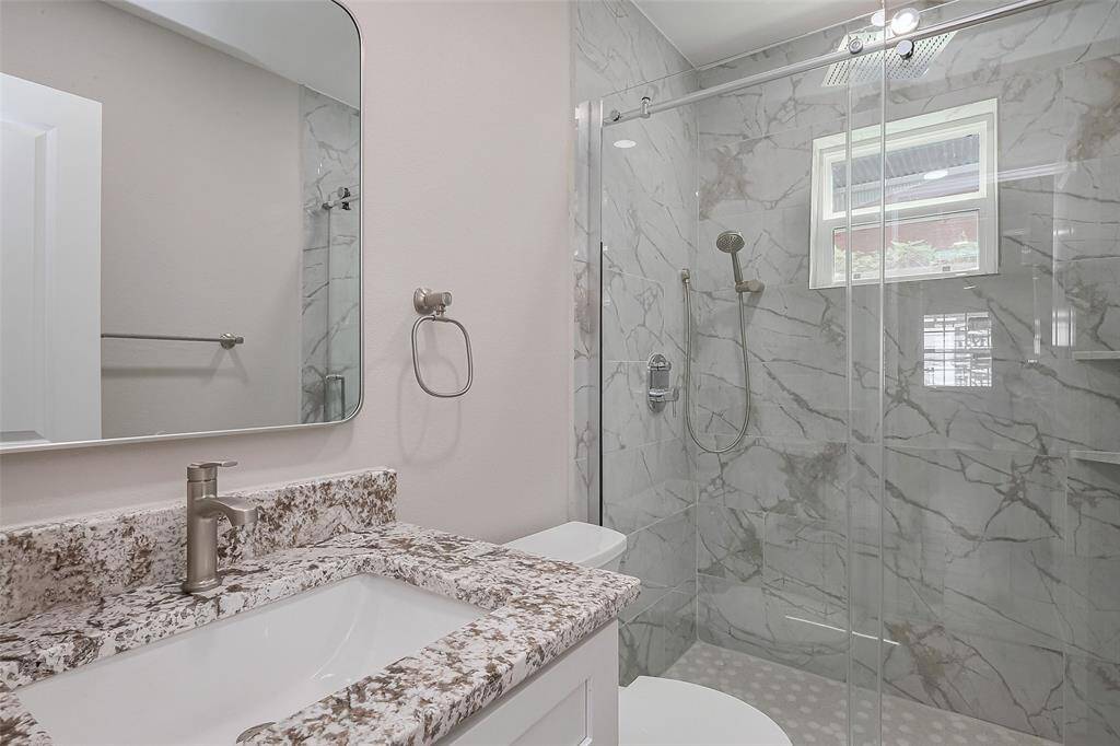 This bathroom features a modern design with a marble-tiled shower, glass doors, and a window for natural light. It includes a granite vanity with a sleek sink and contemporary fixtures.