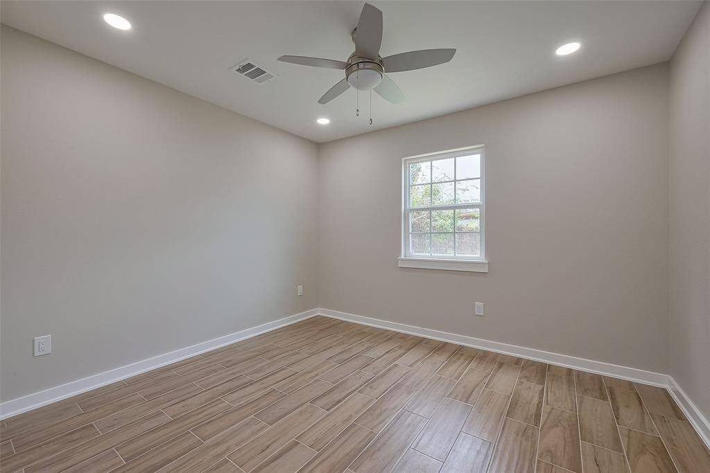 This room features modern wood-look tile flooring, neutral walls, and recessed lighting. A ceiling fan adds comfort, and a window brings in natural light, making it ideal for a cozy bedroom or home office.
