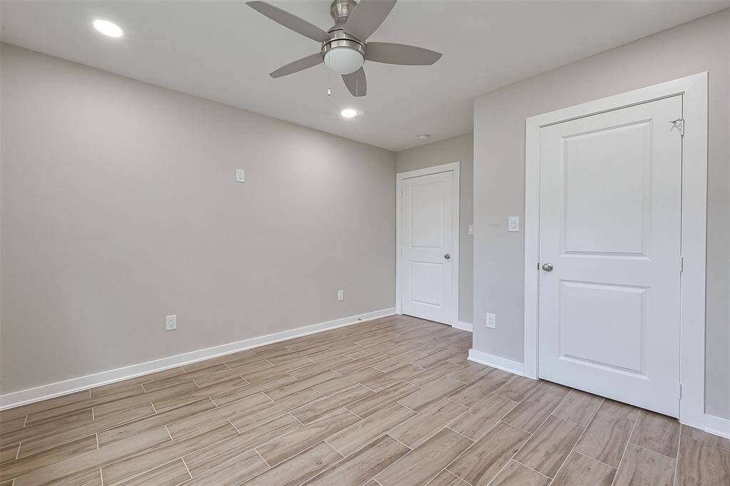 This room features a neutral color palette with light gray walls and wood-look tile flooring. It includes a ceiling fan and recessed lighting, and two white doors, likely for a closet and entry. The space feels modern and versatile.