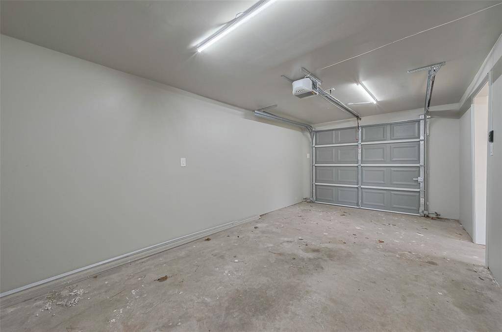 This photo shows a clean, spacious garage with a concrete floor, overhead lighting, and an automatic garage door opener. Ideal for parking or storage.