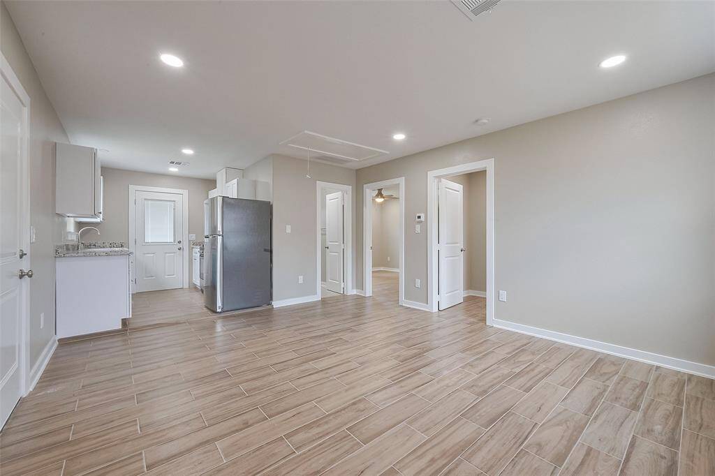 This photo shows a bright, open-concept living area with wood-look tile flooring, recessed lighting, and neutral walls. The space leads into a modern kitchen with granite countertops and stainless steel appliances. There are multiple doors leading to other rooms, enhancing accessibility and flow.