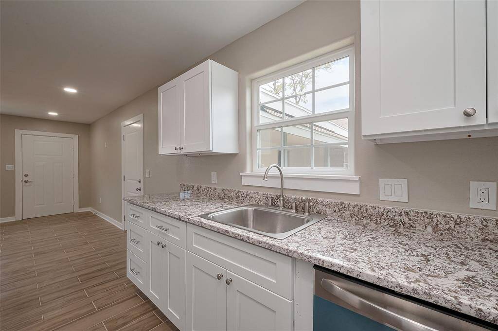This kitchen features modern white cabinetry, granite countertops, and a stainless steel sink. It has a bright, airy feel with natural light from the window and tile flooring for easy maintenance.