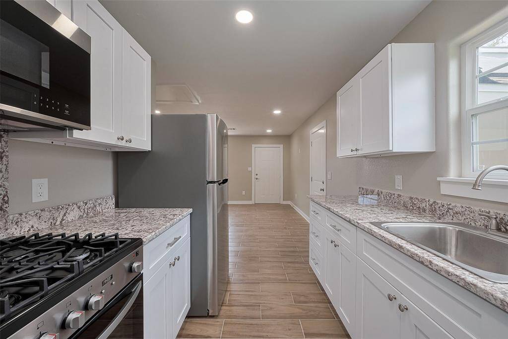 This modern kitchen features sleek white cabinetry, granite countertops, and stainless steel appliances. It has a clean, streamlined design with natural light from a window, and a neutral color palette that enhances the space's brightness.