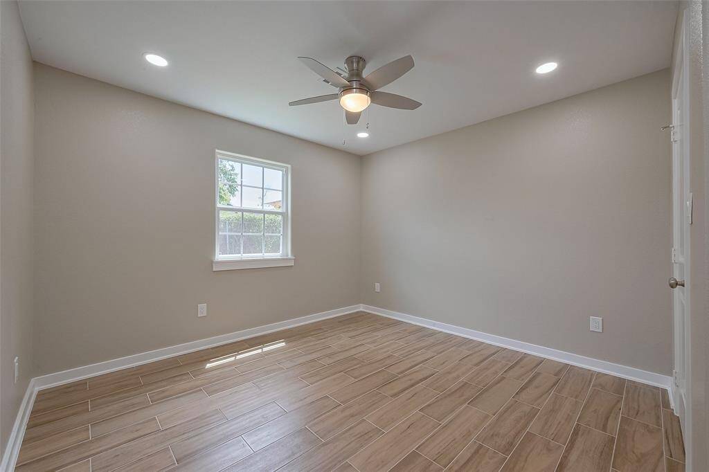 This room features neutral-colored walls, wood-look tile flooring, a ceiling fan with lights, and a window providing natural light. Ideal for a bedroom or office space.