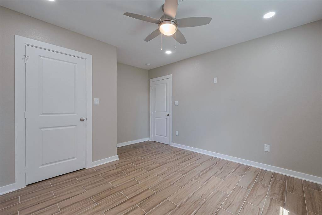 This room features neutral walls and wood-look tile flooring, offering a clean, modern look. It includes a ceiling fan with lighting and recessed lights, providing ample illumination. The space has two white doors, likely for closets or adjoining rooms, enhancing functionality and storage.
