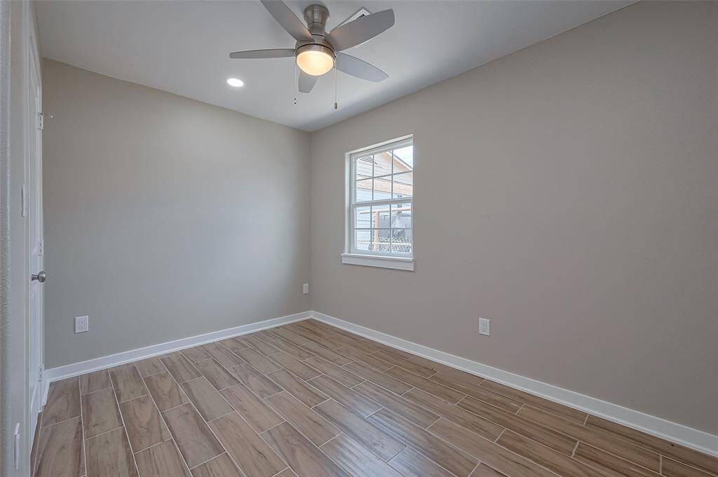 This room features light gray walls, wood-look tile flooring, a window for natural light, and a ceiling fan, creating a cozy and functional space.