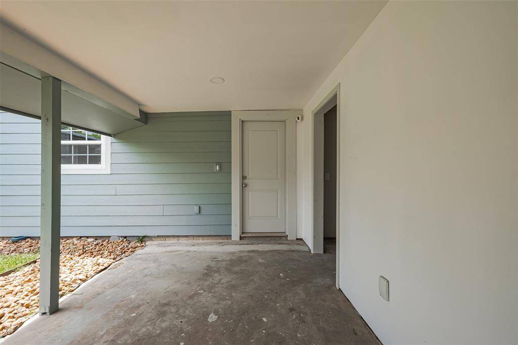 Laundry room with connections  is on the right of the door,  a covered outdoor space with a concrete floor, light blue siding, and a white door leading inside. There's a small window and a neat border of landscaping rocks.