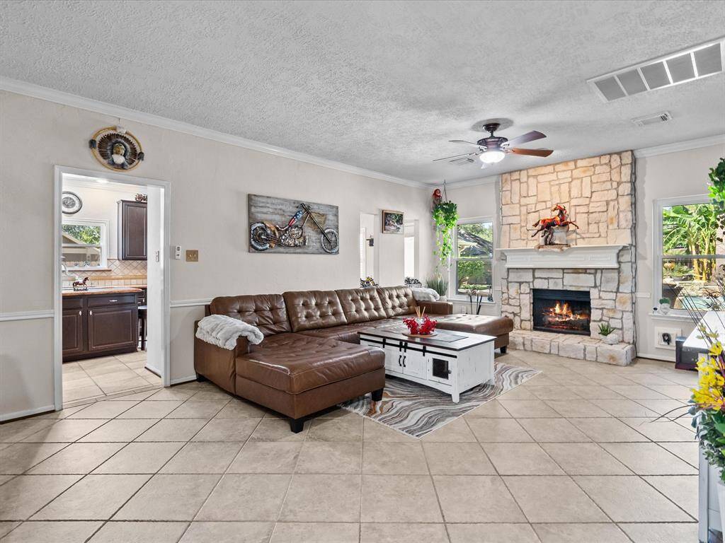 Featuring a rustic stone fireplace with a stone hearth and wood mantle, with both windows offering views of the tropical backyard getaway