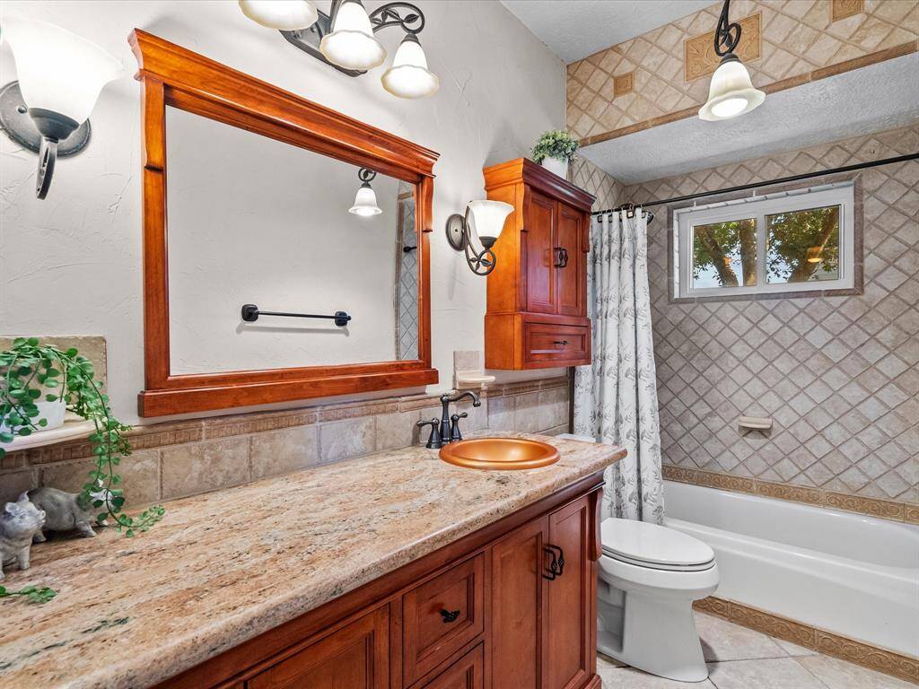 Downstairs full bathroom with granite earth toned vanity and wood cabinetry and copper basin sink
