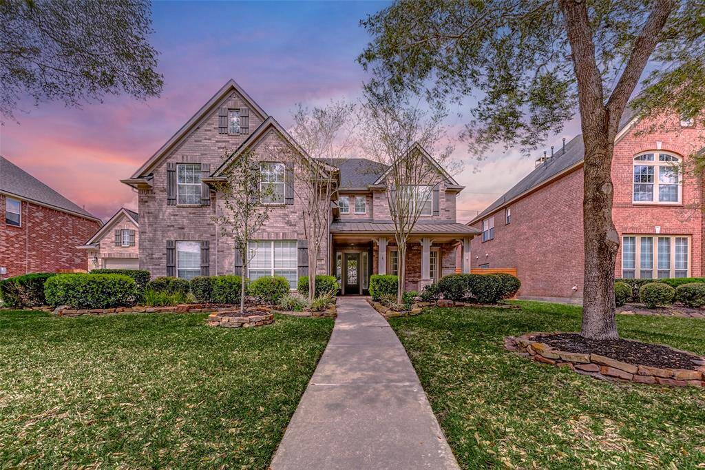 A striking twilight view of the home showcases its graceful architecture, with a long central walkway guiding you through the manicured lawn to the welcoming front porch. Neatly arranged plant beds and a mix of young and mature trees add freshness and foliage to the surroundings.