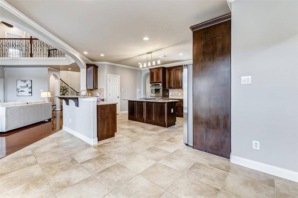 A chef’s dream layout, the kitchen boasts an abundance of rich cabinetry and expansive countertops for effortless prep and storage. A raised bar subtly separates the space from the adjacent living room, while a generous opening above provides continuous sightlines and connection.