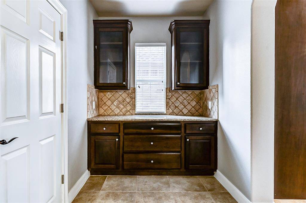 Tucked between kitchen and dining, the elegant butler’s pantry is bathed in natural light from a tall window and flanked by overhead glass-front cabinets.