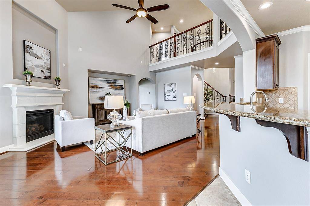 This spacious living area impresses with soaring ceilings, a stylish fireplace, and a full wall of towering windows that fill the room with daylight. The upper-level overlook, detailed with wrought iron railings, and thoughtful architectural niches elevate the sense of openness and design.