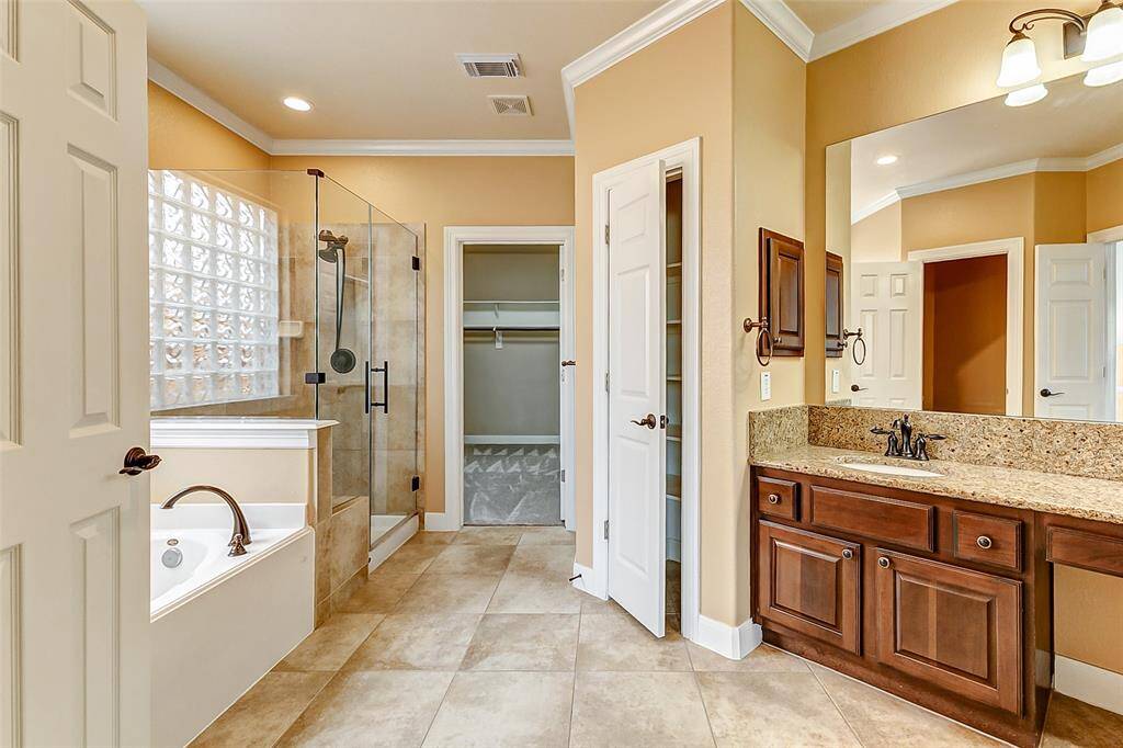 The en suite bath is a tranquil haven, boasting dual vanities with abundant storage, broad mirrors, and stylish lighting. A soaking tub sits beside a glass-enclosed shower, offering both indulgence and practicality.