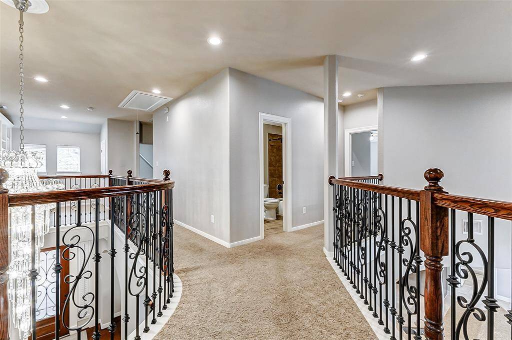 Overlooking both the living room and entry below, this carpeted upstairs landing features wrought iron railings and recessed lighting. It connects seamlessly to the secondary bedrooms, offering a sense of spaciousness and flow.