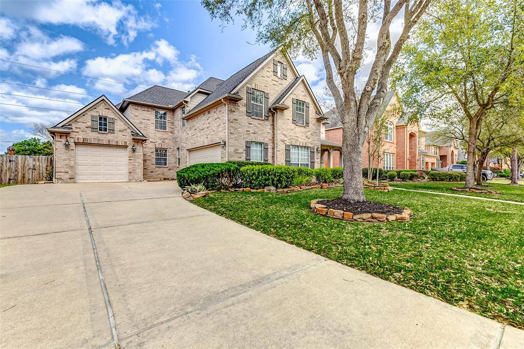 Bathed in natural daylight, the home's timeless charm is on full display. A wide, pristine driveway curves toward the side-entry garage, skirting the expansive green lawn and echoing the property's generous quarter-acre scale.