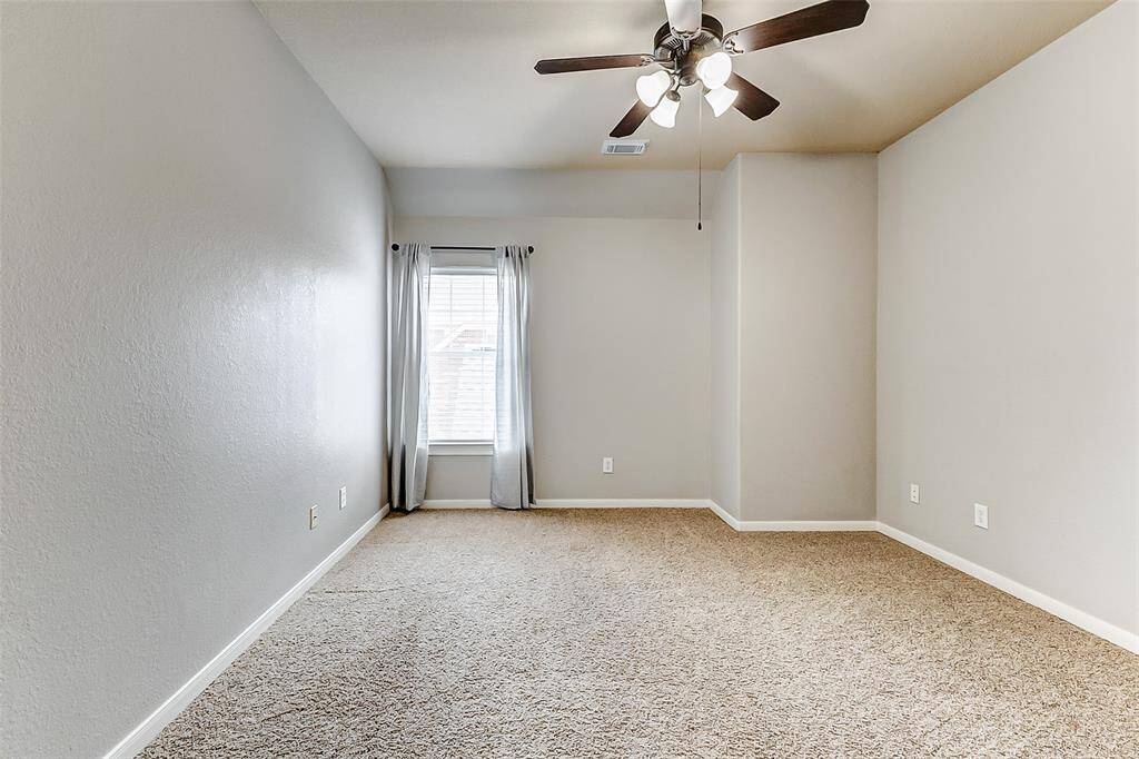 A bright and welcoming upstairs bedroom, featuring soft neutral tones, a tall window for ample light, and a ceiling fan for added comfort. A large closet provides practical storage.