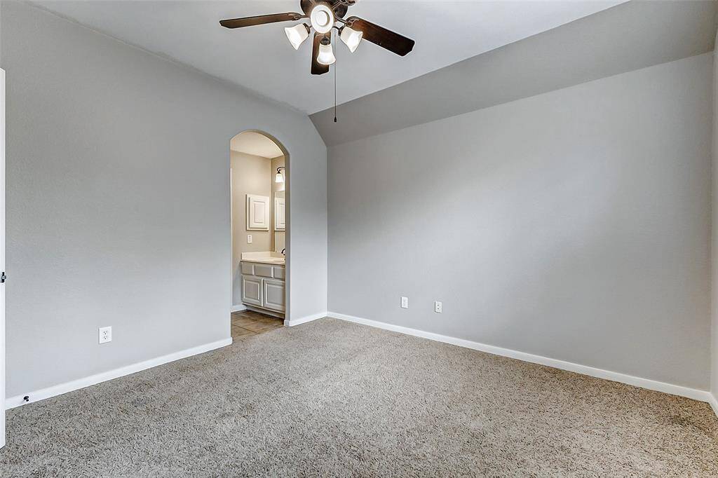 This charming bedroom includes a gentle sloped ceiling and soft carpeting, with a ceiling fan overhead. An arched entryway leads to a private vanity area, offering both function and character.