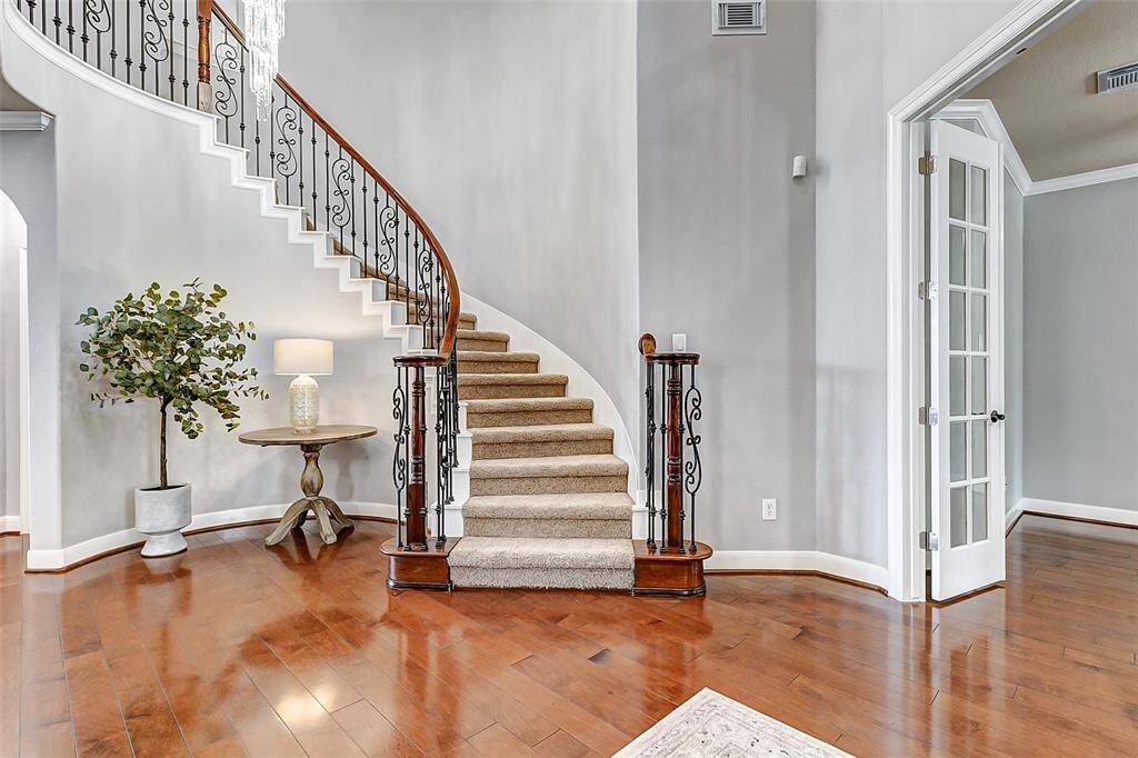 Step into a luminous foyer with a sweeping staircase that curves upward in soft carpeted elegance. Double French doors open into a private study, while to the left, the formal dining area beckons. The space opens up with sightlines into the main living room, drawing you deeper into the home.