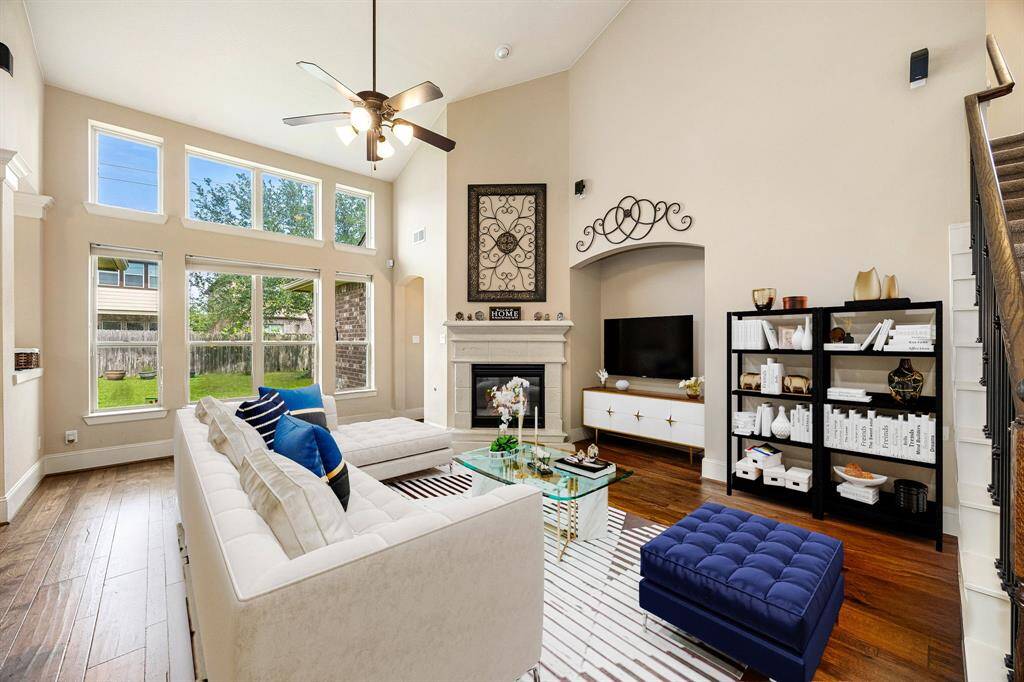 This living room is more like a GREAT room featuring a stunning fireplace with mantel detailing, custom paint, soaring high ceiling, recessed lighting, dark stained ceiling fan, and an amazing wall of windows providing a lovely view of your backyard to keep an eye out on the kids or pets playing. *Virtually Staged