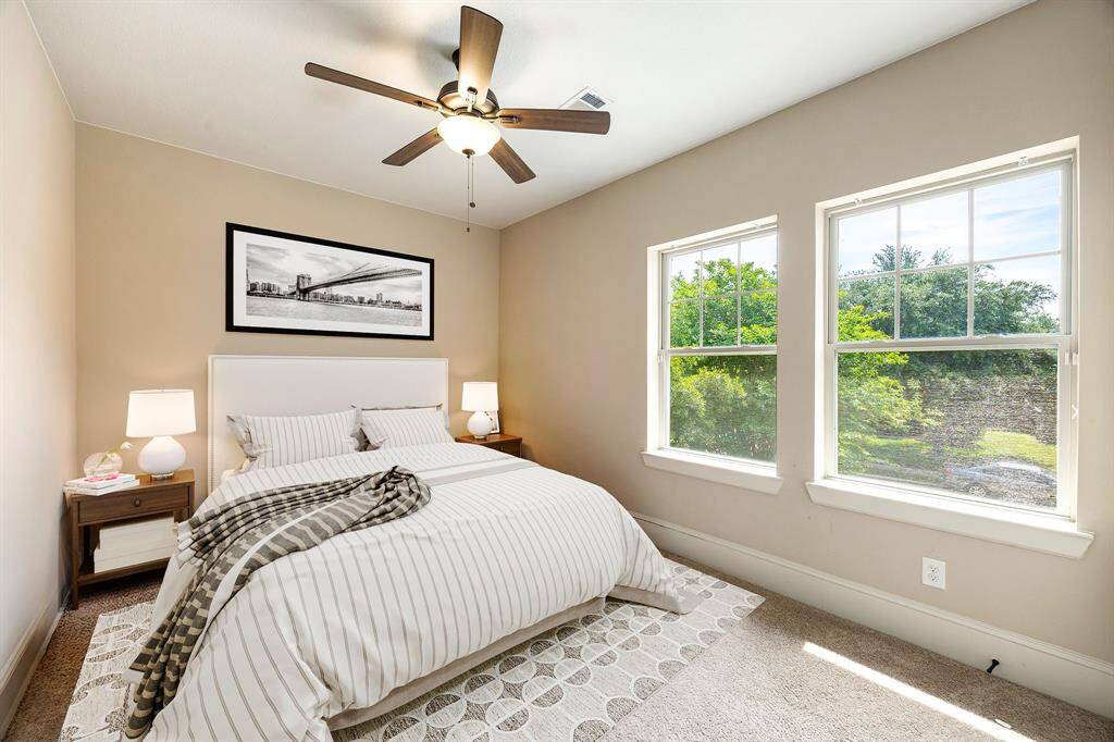 This secondary bedroom offers comfort and style with plush carpeting, custom paint, a dark-stained ceiling fan with built-in lighting, and a large window fitted with privacy blinds for natural light and tranquility. *Virtually Staged