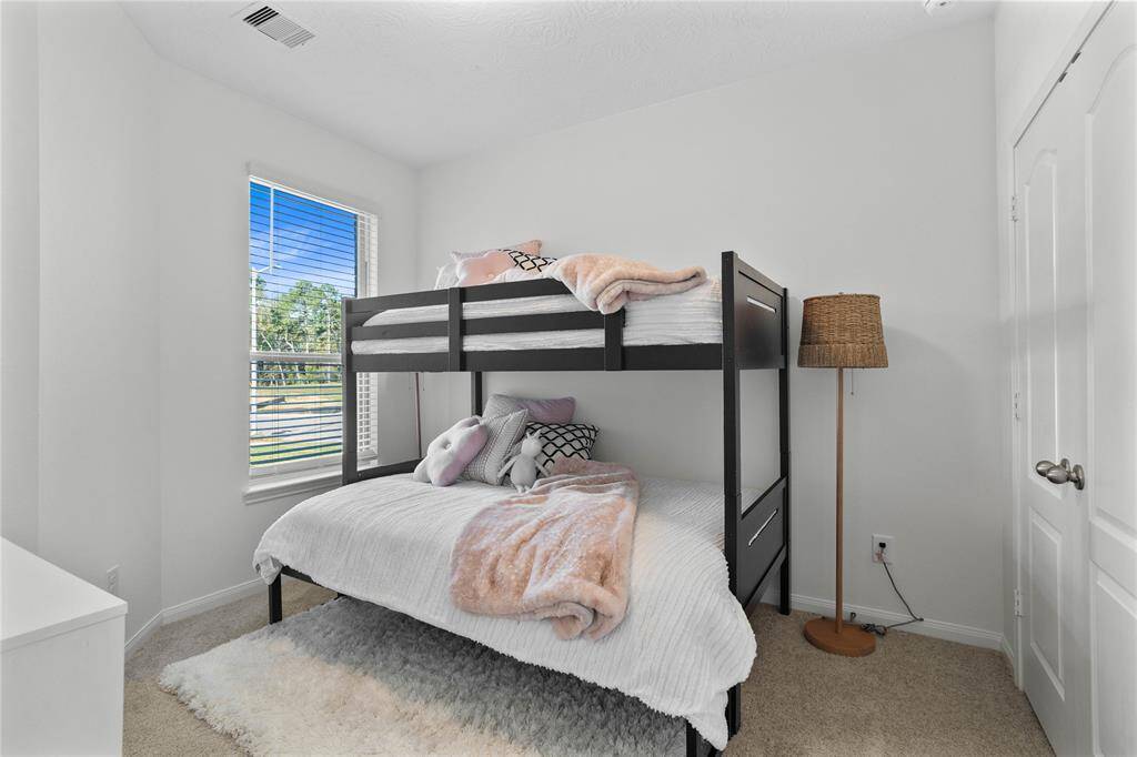 Secondary bedroom features plush carpet, high ceilings, ample closet space, and a large window with privacy blinds.