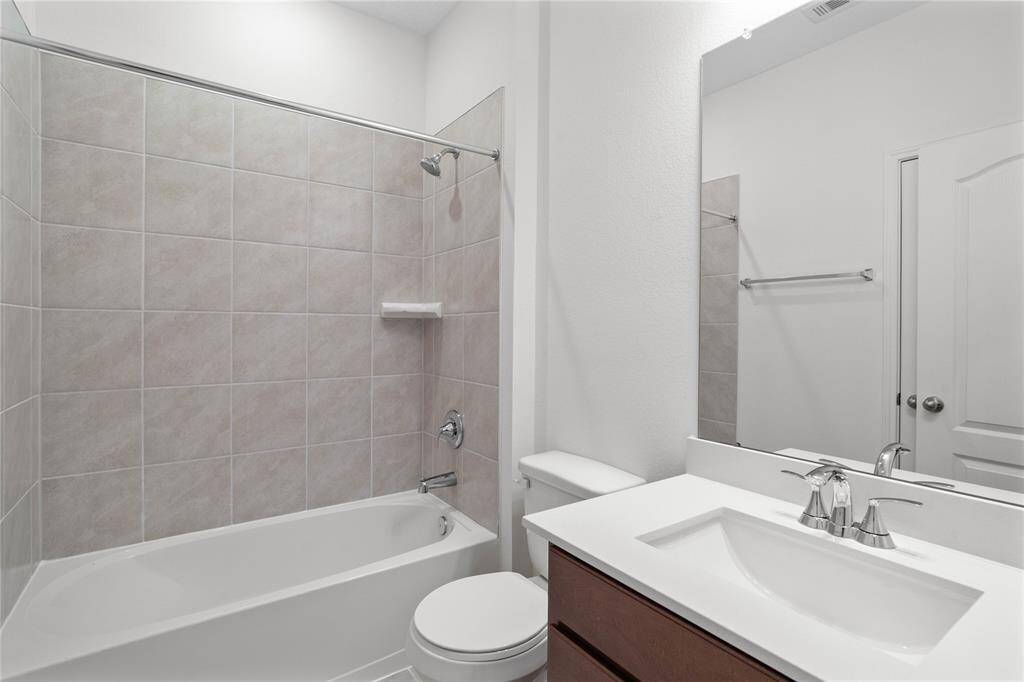 Secondary bathroom features stained cabinets, neutral paint, shower/tub combo with tile surround, large mirror, tile floors, and sleek fixtures and modern finishes.