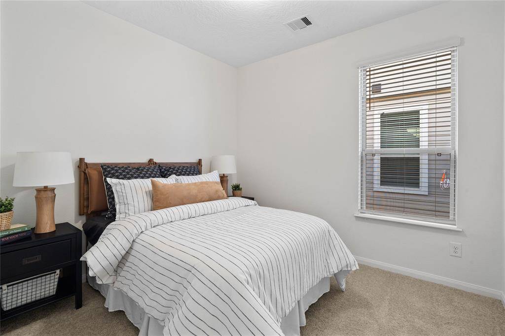 Secondary bedroom features plush carpet, high ceilings, ample closet space, and a large window with privacy blinds.