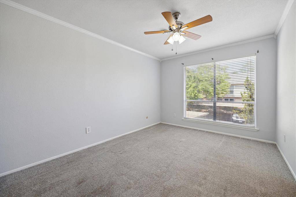 Secondary bedroom features neutral walls, carpeted flooring, a ceiling fan with lights, and a large window with blinds offering plenty of natural light.