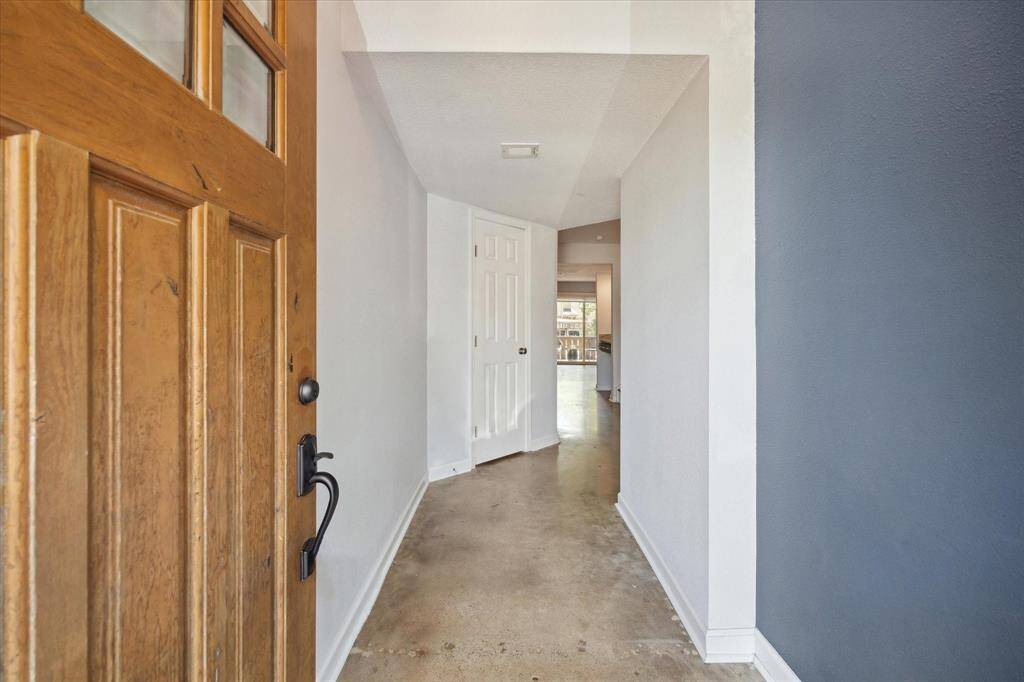 This welcoming entryway features a solid wooden door, stained concrete flooring, and neutral walls, leading to a bright, open living area.