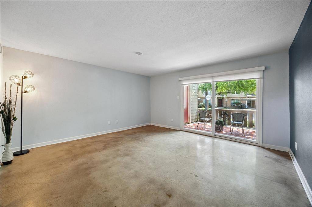 Spacious living room, featuring a large sliding glass door that opens to a private outdoor patio. The room is well-lit with natural light and has a neutral color palette.